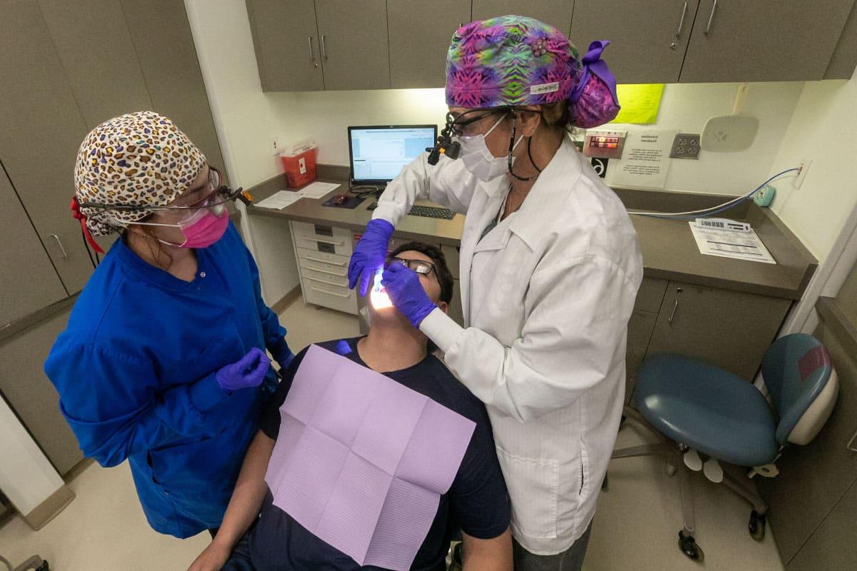 两名太阳集团娱乐场登陆网站的牙科学生正在治疗一名病人