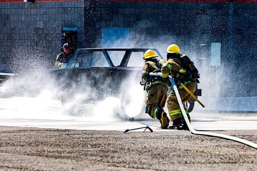 两名消防员拖着一根水管走向一辆着火的汽车